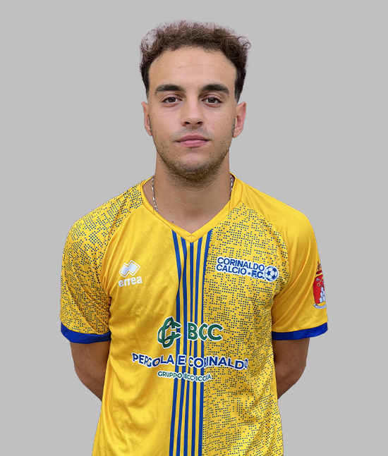 Giocatore di calcio in posa frontale con divisa gialla Corinaldo Calcio F.C., dettagli blu e sponsor visibili, su sfondo grigio neutro